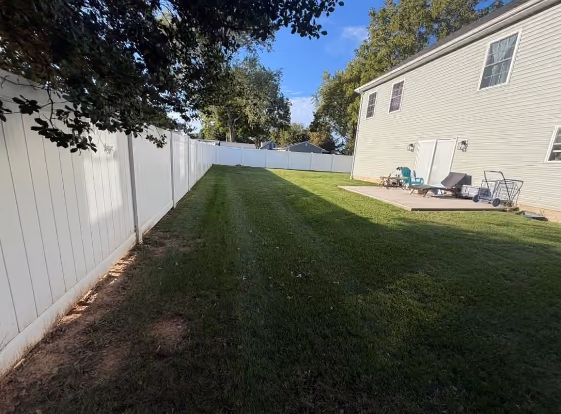 Mowed back lawn beside a white fence and the rear of a house