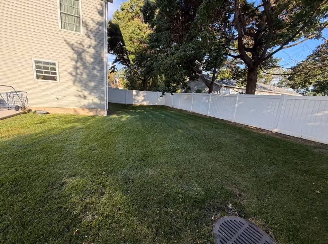 Mowed side lawn between a house and a white fence