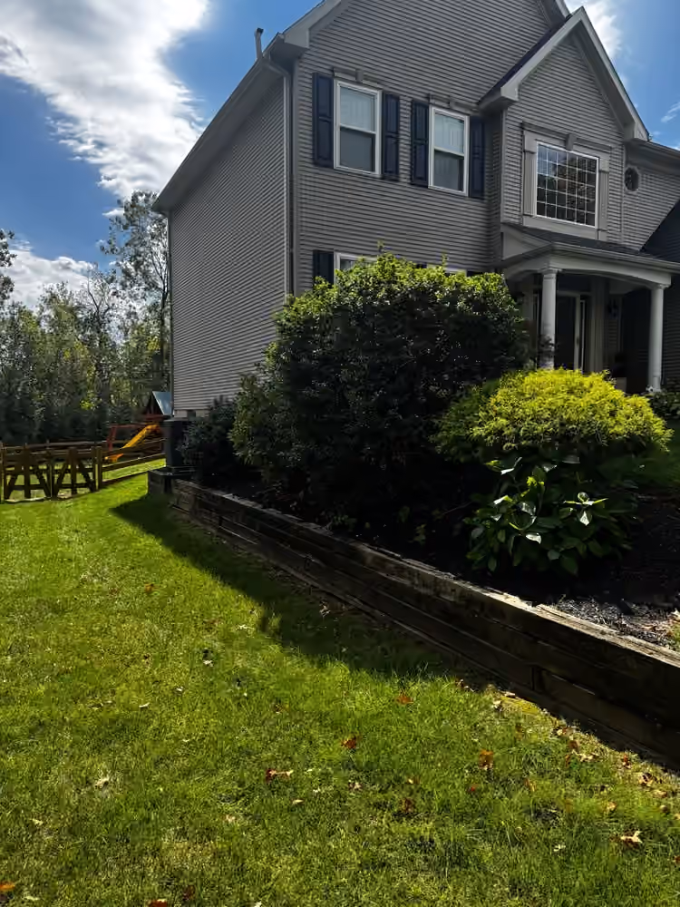 Freshly mulched bed behind a timber retaining wall at the front corner of a house