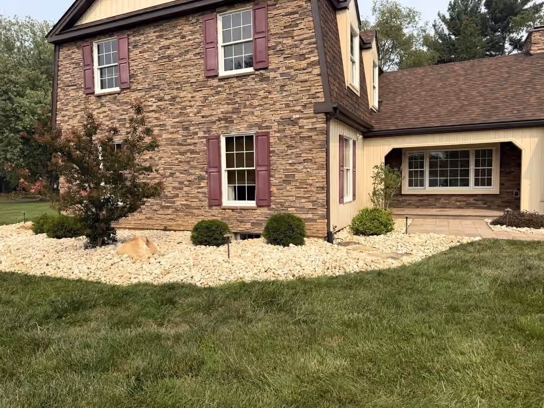 River rock bed wrapping the corner of the house past a small maple