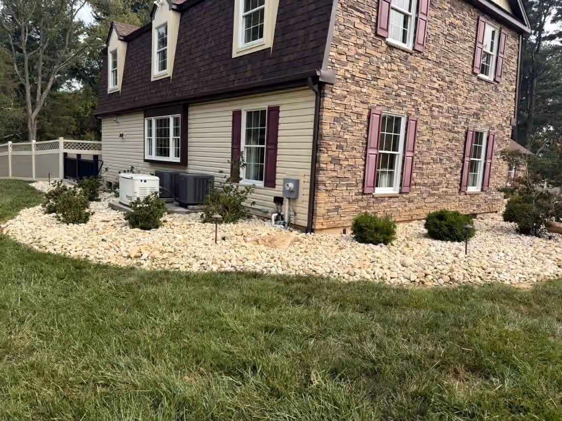 Curved river rock bed with low shrubs along the front of a stone and siding house