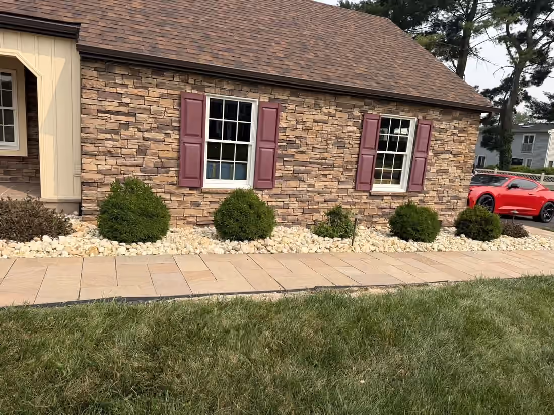 Rounded shrubs in a river rock bed between the house and a paver front walk