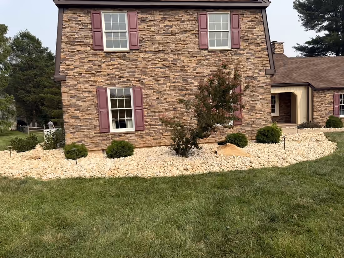 River rock bed with rounded shrubs and a small red maple under the gable end