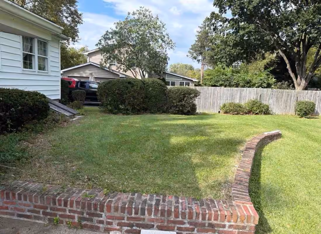 Mowed side lawn between a clipped hedge and a curved brick retaining wall