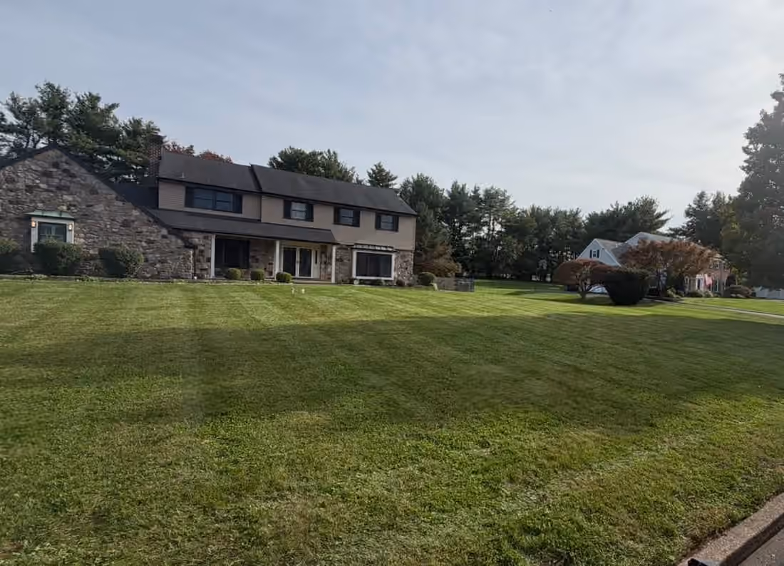 Wide front lawn mowed in light and dark stripes in front of a stone and siding house